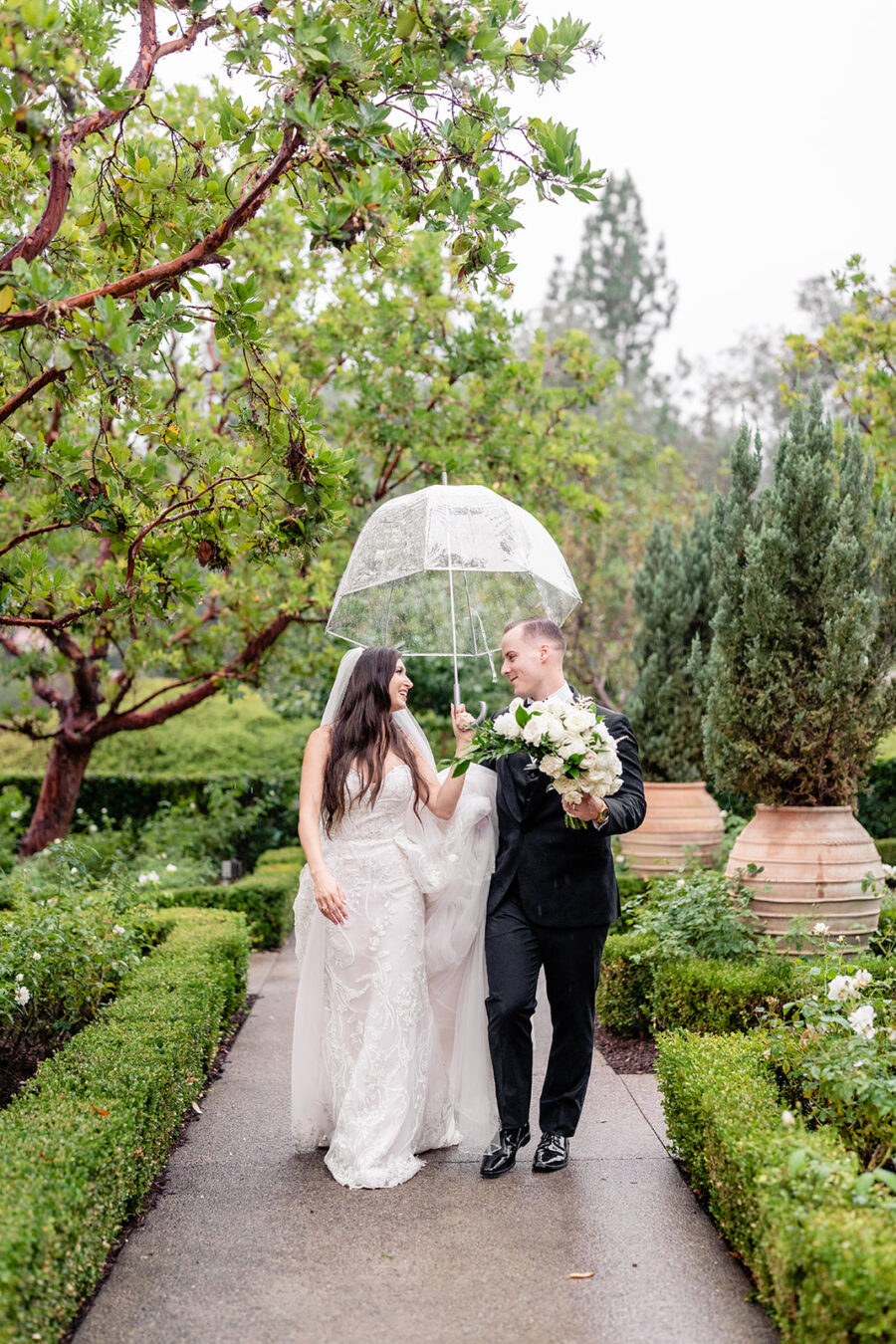 Bride and groom walking together under an umbrella during their rainy wedding day at Rancho Bernardo Inn Wedding venue in San Diego