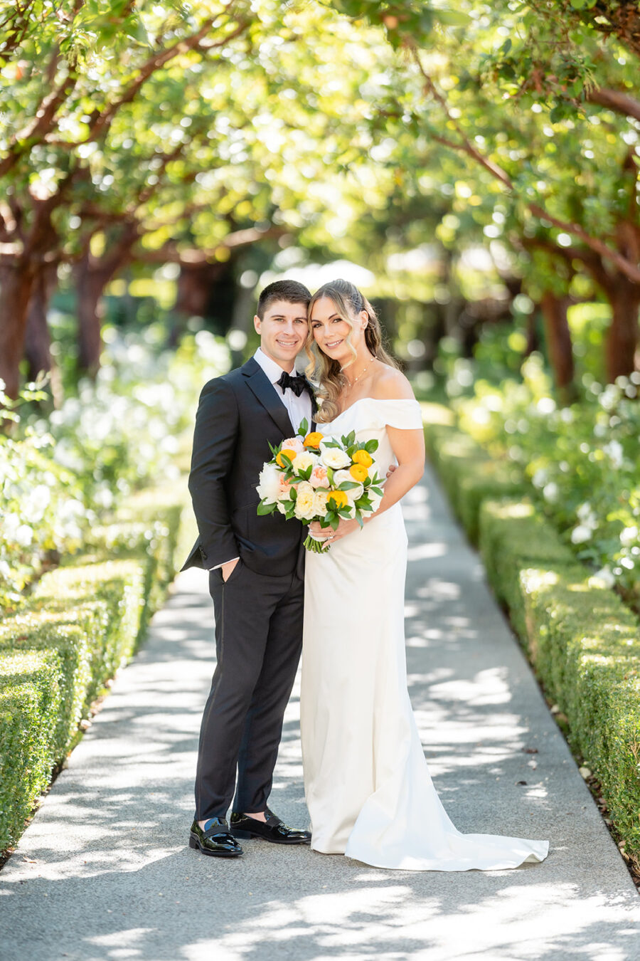 Bride and Groom posing together in a walkway under the trees near Aragon Lawn Wedding Venue in San Diego.